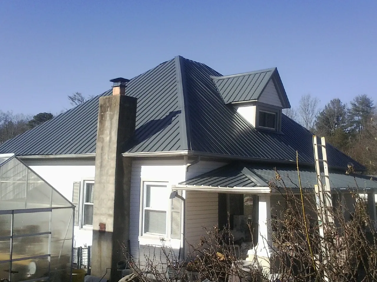 Dark blue standing seam metal roof on a white farmhouse with dormer — Slate & Tile Roof Repair by Roofing Brothers in Shippingport