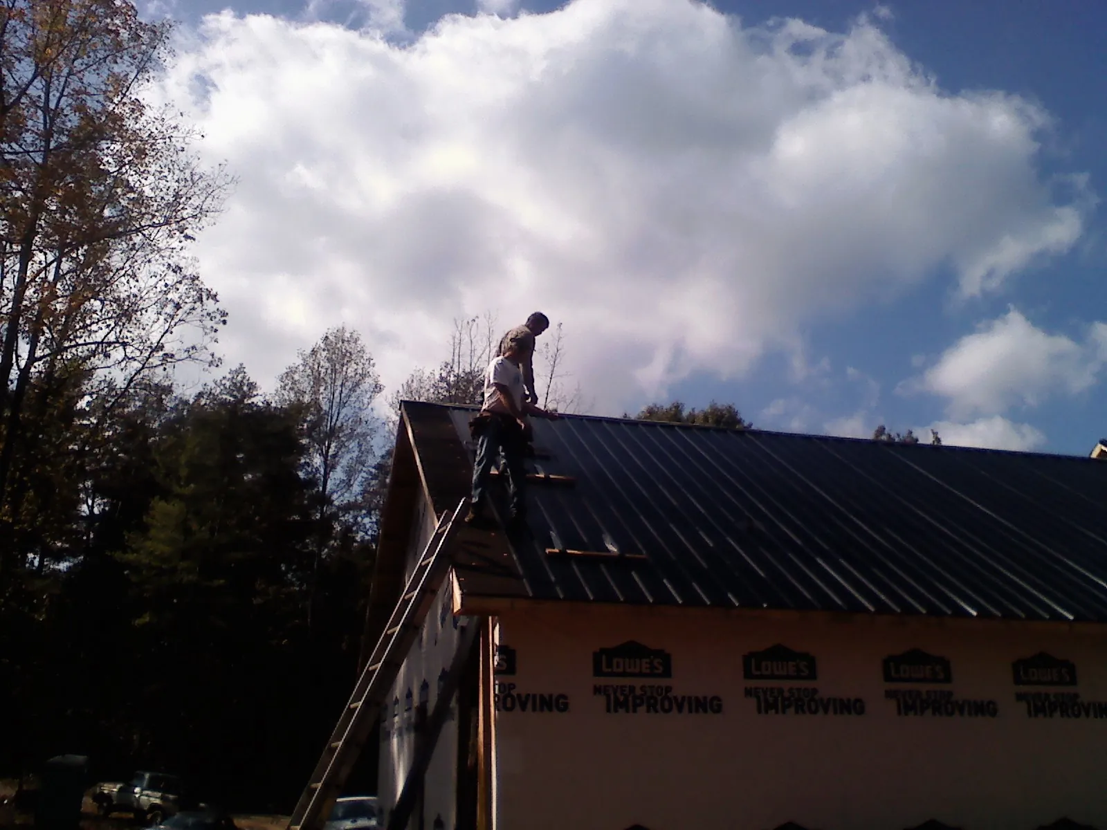 Roofer fastening dark metal panels high against a cloudy sky, from a Roof Inspection job in Shippingport
