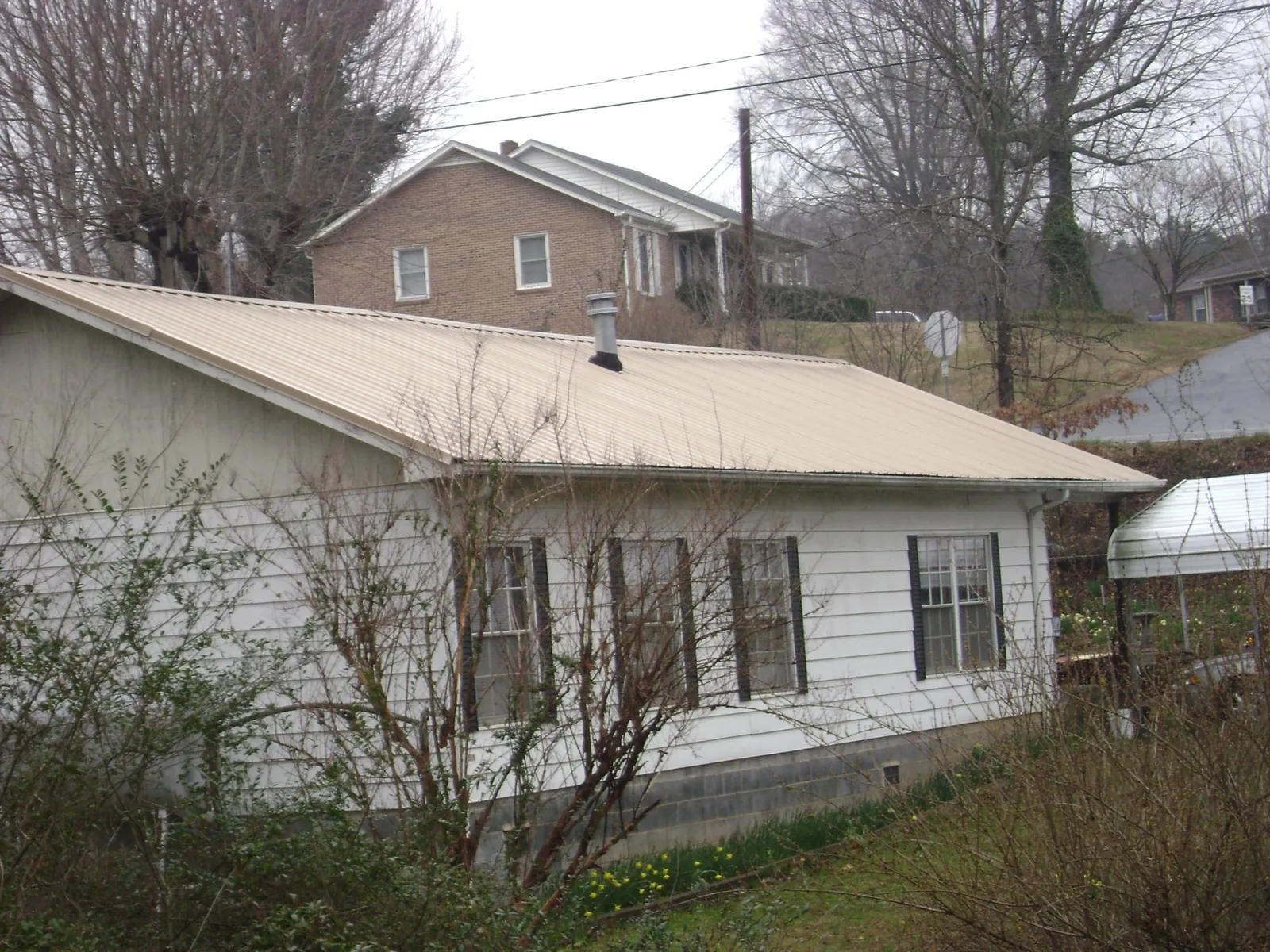 Tan metal roof on a white sided house set into a hillside — Commercial Roofing by Roofing Brothers in Shippingport